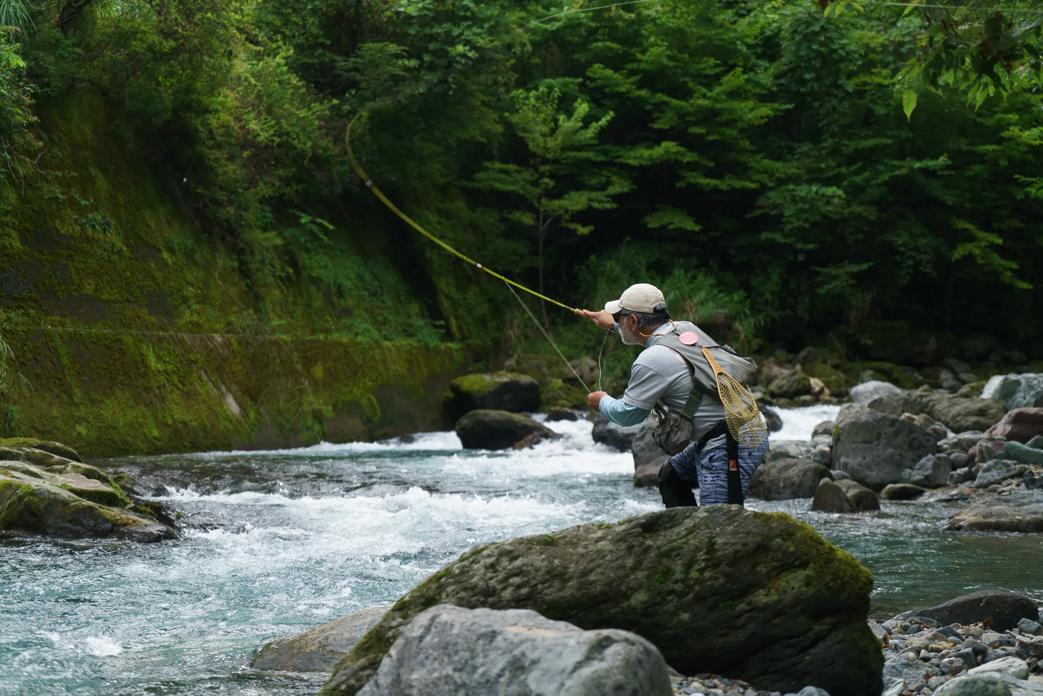 An angler casting a bamboo fly rod on a green mountain stream